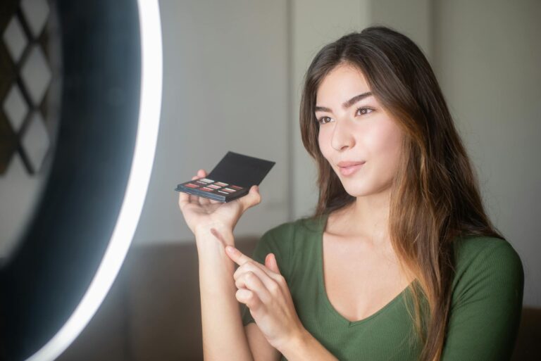 Young woman influencer applying makeup in well-lit indoor setting, showcasing beauty products.
